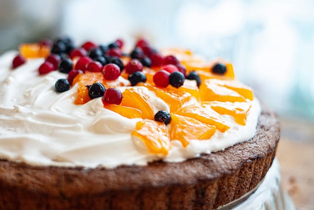 Feature Image - Whipped cream frosting on top of a cake with blueberries and cherries garnish