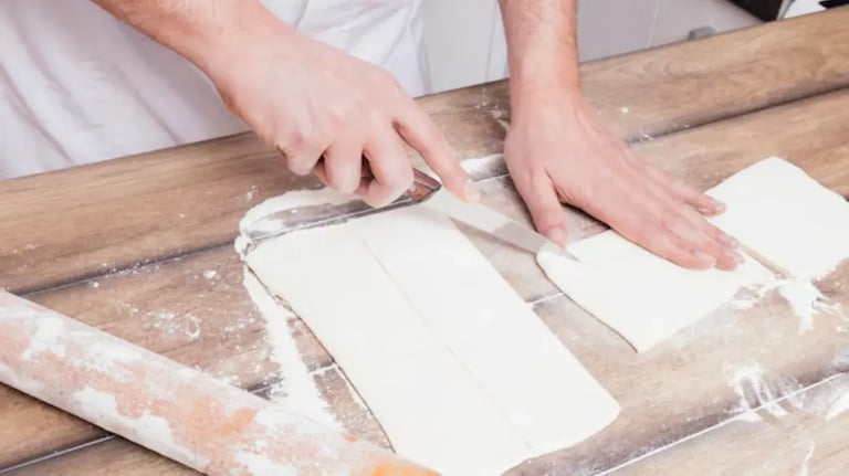 Feature Image - Person cutting homemade puff pastry sheets on a floured wooden surface using a kitchen knife