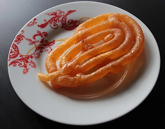 Feature Image - A piece of jalebi dessert made with rice flour, water, and sugar syrup